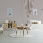 Spacious living room with wooden table on white carpet, rustic cupboard and grey sofa near open bedroom